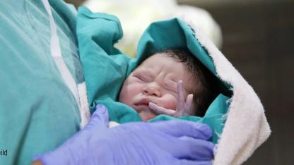 Neugeborenes Baby in den Armen einer Pflegekraft